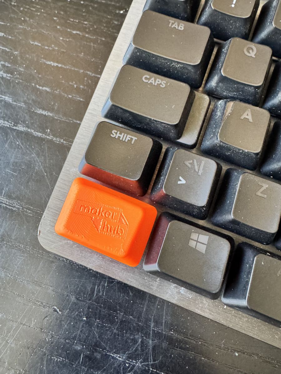 Orange 3D-printet keycap med MakerHub-logo