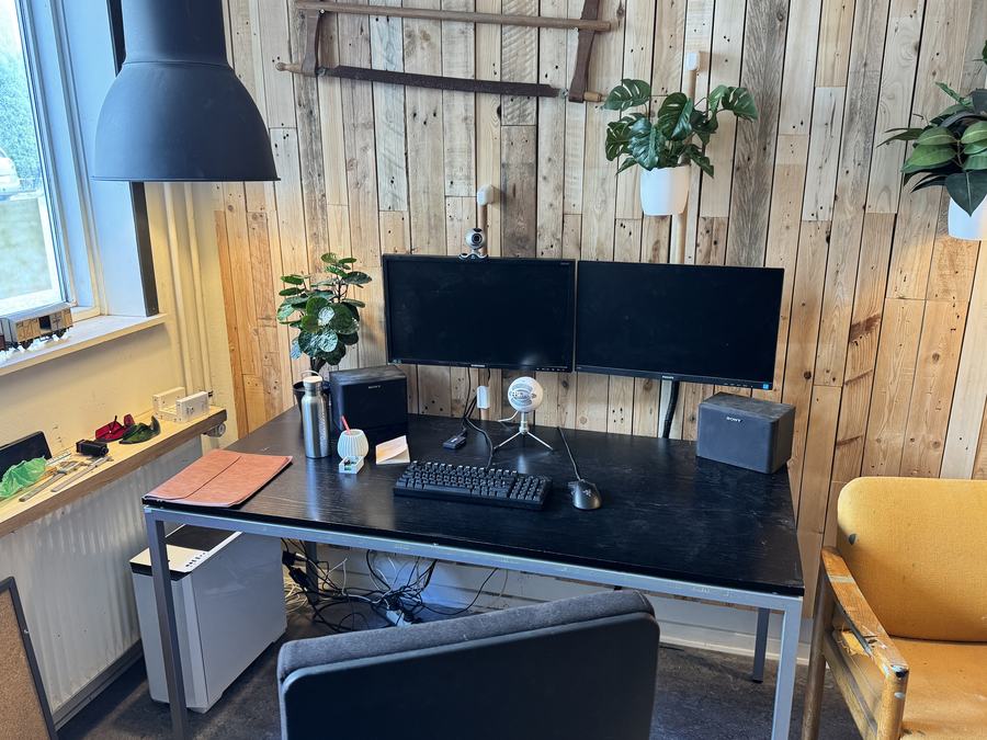 Arbejdsbord med to skærme mod en væg af genbrugstræ